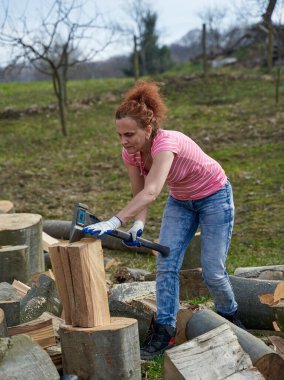 Kadın çiftçi arka bahçede yakacak odun bulmak için kayın kütüklerini kırıyor.