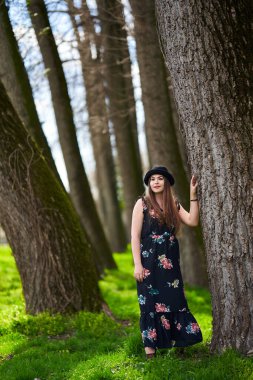 Genç bayan, baharın başında parkta gezintiden zevk alıyor. Büyük ağaçların arasında taze yeşil çimenler.