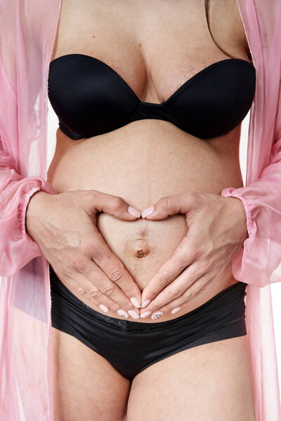 Беременная женщина в черном нижнем белье позирует на белом фоне