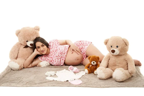 毛毯上挂着玩具和婴儿衣服的孕妇 免版税图库图片