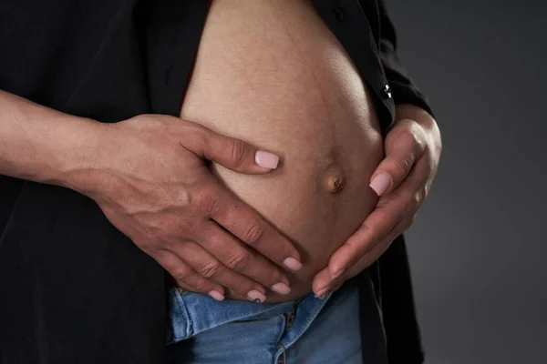 妊娠中の女性で青ジーンズとボタンなし黒シャツ上の灰色の背景 — ストック写真