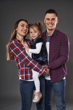 Anne, baba ve küçük kızıyla mutlu bir aile. Stüdyo, gri arka planda çekim yapıyor.