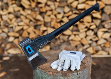 Bir odun yığınının yanında bir oduncunun baltası ve koruyucu eldivenleri.