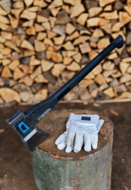 Bir odun yığınının yanında bir oduncunun baltası ve koruyucu eldivenleri.