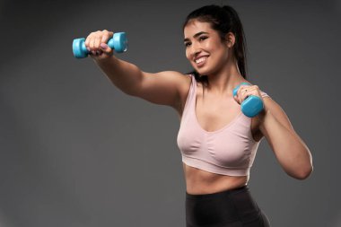 Mutlu ve iri yarı İspanyol kadın küçük dambıllarla spor yapıyor.