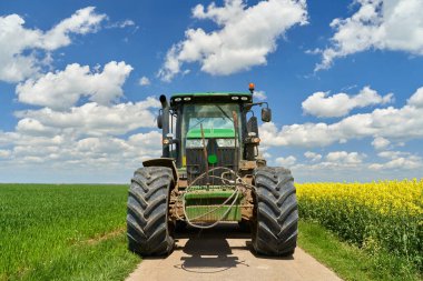 Bir kanola ile mavi gökyüzünün altında bulutlu buğday tarlası arasında büyük bir traktörle manzara