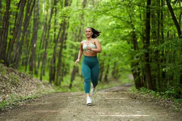 美丽又大的女跑步者在森林的土路上奔跑 — 图库照片