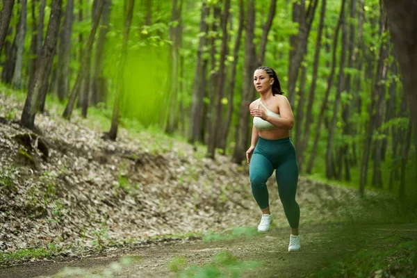 森の未舗装の道を走る美しいプラスサイズのランナー女性 — ストック写真