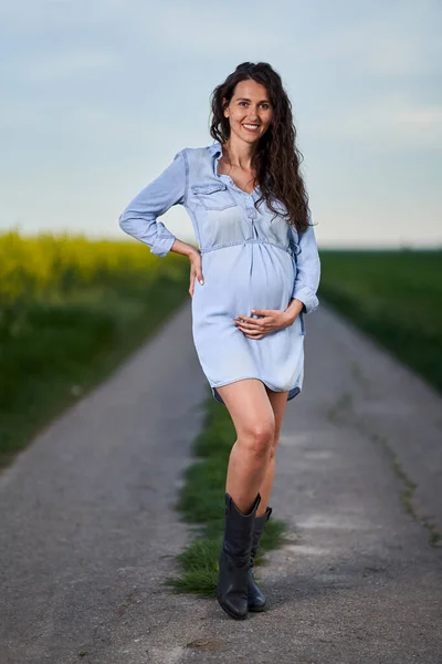 在小麦和油菜地之间的路上怀孕的妇女 — 图库照片