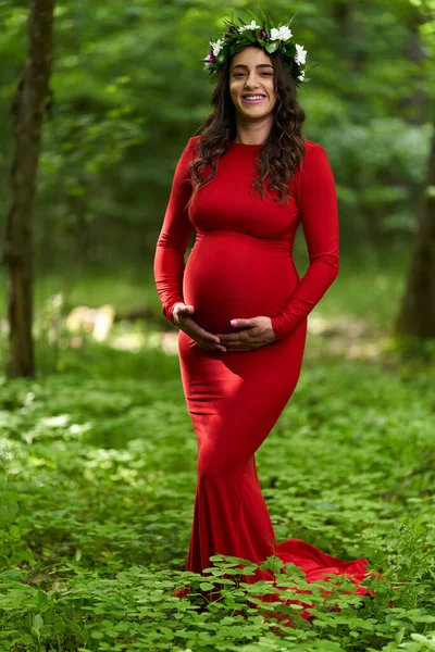 夏に落葉樹林で長い赤いドレスを着た美しい若いヒスパニック系妊婦の肖像画 — ストック写真