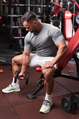 Vücut geliştirici, spor salonundaki halterlerle biseps kıvırma egzersizi yapıyor.