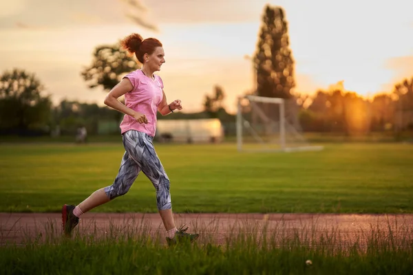 日落时在城里的一条跑道上奔跑的女人 — 图库照片