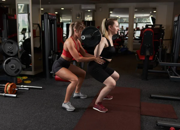 Kvindelig Personlig Træner Hjælper Ung Kvinde Gør Vægtstang Squats Gymnastiksalen - Stock-foto