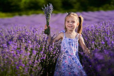 Bahçenin ortasında elinde lavanta buketi tutan sevimli küçük kız.