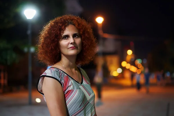 夜色中城市里一头卷发红头发女人的选择性聚焦画像 — 图库照片