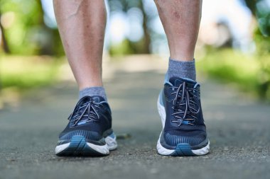 Parktaki bir ara sokakta koşan bir maraton koşucusunun kaslı baldırlarına ve ayakkabılarına yakından bakın.