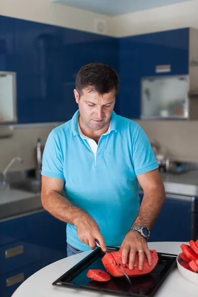 Caucasian man in the kitchen slicing watermelon — Stock Photo, Image