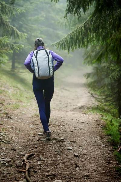 Kvinna med ryggsäck vandring in i skogen — Stockfoto