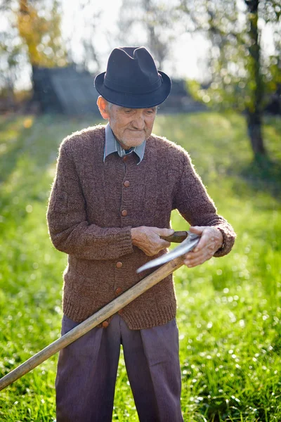 Vecchio agricoltore affilatura falce — Foto Stock