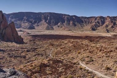 Önünde Llano de Ucanca ile Cumbre de Ucanca olarak bilinen Las Canadas Caldera 'nın geniş manzarası ve kurak volkanik araziyi kesen bir yürüyüş yolu.