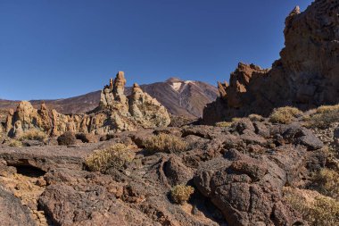 Teide Dağı, Tenerife 'deki Tenerife Ulusal Parkı' nda açık mavi bir gökyüzünün altında görülebilen Roques de Garcia volkanik oluşumları ve güneşli kuleler.