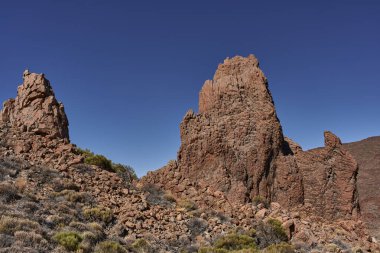 Jagged volkanik kayaların gündüz görüşü ve katmanlı oluşumlar Tenerife 'deki Roques de Garcia' da açık mavi gökyüzünün altında kurak araziden yükseliyor.