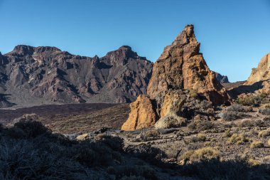 Kurak çalıların ve dağların arasında yükselen engebeli volkanik kaya oluşumları Tenerife 'deki Roques de Garcia' da açık mavi gökyüzünün altında sınırlandırılmış bir patika.