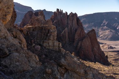 Sarsıntılı volkanik kayalar ve katmanlı oluşumlar Tenerife 'deki Roques de Garcia' da açık mavi gökyüzünün altında kurak araziden yükselir.