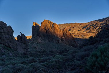 Roques de Garcia 'nın volkanik kaya oluşumları engebeli lav arazisi ve açık mavi gökyüzü ile sabah güneşiyle aydınlatılıyor.