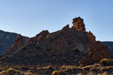 Roques de Garcia 'nın volkanik oluşumları engebeli lav arazisi ve açık mavi gökyüzü ile sabah güneşiyle aydınlanıyor.