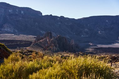 Roques de Garcia 'nın volkanik oluşumları engebeli lav arazisi ve açık mavi gökyüzü ile sabah güneşiyle aydınlanıyor.