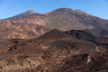 Narices del Teide, Pico Viejo ve Pico del Teide 'yi gösteren engebeli volkanik manzara açık mavi gökyüzü altında keskin kayalık tepeler ve lav tarlaları ile hizalanmıştır.