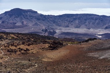 Volkanik yamaç ve patikalı geniş manzara, Llano de Ucanca ovası ve arka planda Las Canadas caldera çemberi sol üstte Guajara Dağı ile birlikte.