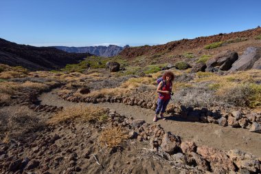 Kadın yürüyüşçü, arka planda Las Canadas Caldera ile Pico Viejo 'ya doğru yokuş yukarı yürüyor.