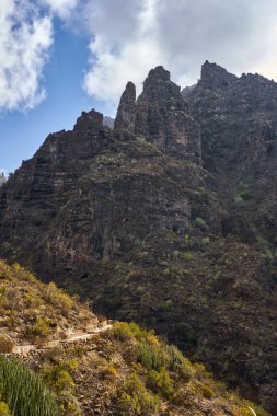 Dik volkanik kayalıklar ve sabah ışığı altında engebeli Barranco del Infino arazisinde dolanan dar bir patika.