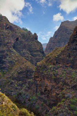 Tuff ve koyu bazalt yatakları kuru bitki örtüsüyle çevrili dramatik kaya yüzeyini oluşturur..