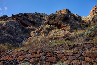 Anaga 'da taş terasları, seyrek astropikal bitki örtüsü ve açık mavi gökyüzü olan volkanik kayalık bir yamaç.