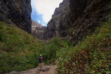 Dişi yürüyüşçü, yüksek volkanik kayalıklara ve Barranco del Infierno 'nun dramatik dar vadisindeki kaya zirvesine bakıyor.