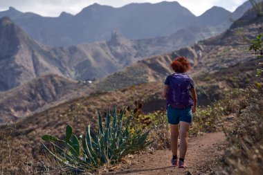 Mor sırt çantalı kadın yürüyüşçü Anaga Dağları 'ndaki teraslı vadilere ve volkanik tepelere bakan dağ yolunda yürüyor.