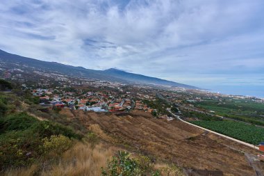 Tarım tarlaları ve Tenerife Kanarya Adaları 'ndaki bulutlu gökyüzünün altında görünen Teide Dağı volkanı ile La Orotava kasabasının panoramik manzarası