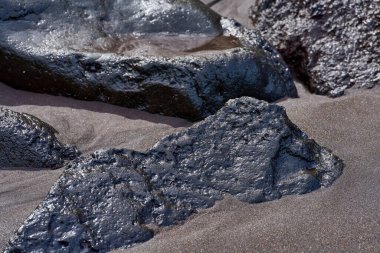 Tenerife Kanarya Adaları 'ndaki El Bollullo plajında kısmen kumla kaplı kara volkanik kaya ve kayalar.