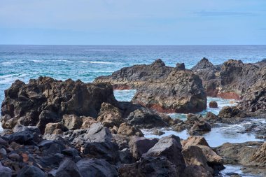Tenerife Kanarya Adaları 'ndaki El Bollullo sahilinde gelgit havuzları ve okyanus suyuyla volkanik kaya oluşumları.