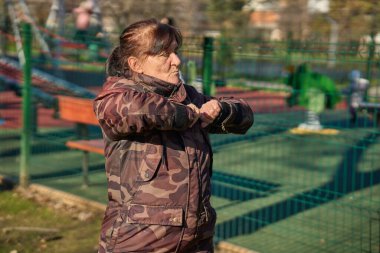 Dışarıda parkta egzersiz yaparken kollarını göğsüne uzatan son sınıf öğrencisi bir kadın.