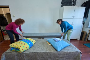 Uzanabilir bir kanepeyi oturma odasında uyuyan bir yatağa dönüştürmek için birlikte çalışan iki kadın.