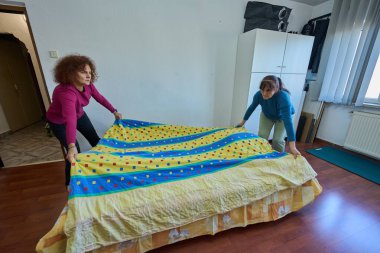 Genişletilebilir bir kanepeyi dairelerde uyuyan bir yatağa çevirmeye çalışan kadınlar.