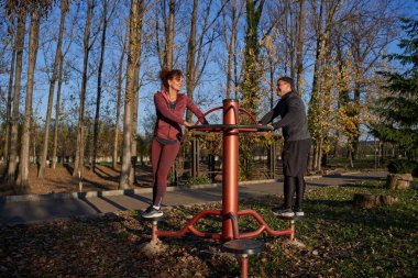 Sonbahar parkında spor salonunda belden bükme makinesinde birbirine bakan neşeli çift.