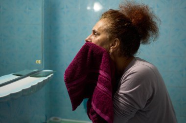 Kadın sabah hijyen rutininin bir parçası olarak yüzünü mor havluyla kurular.