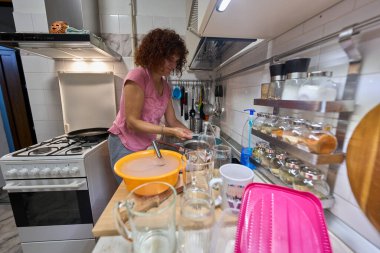 Kadın, yemek yaptıktan sonra etrafı bardaklar ve kâselerle çevrili mutfak lavabosunda bulaşık yıkıyor.