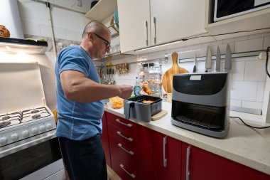 Mavi tişörtlü orta yaşlı bir adam mutfak tezgahına baharatlı et koyuyor.