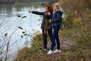 İki orta yaşlı kadın arkadaş nehir kenarında kuş gözlüyor su kuşlarını arıyorlar.